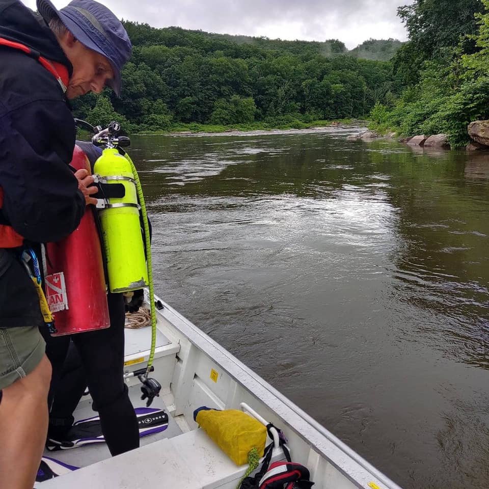 Stephen Stuart, a member of the Narrowsburg Fire Department, works as a tender assisting the diver with their air tanks and gear as they ready for a recovery search on the Upper Delaware River in June. The boat is positioned upriver from the point the person was last seen...